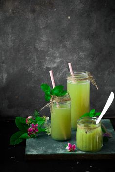 two jars filled with green liquid next to flowers