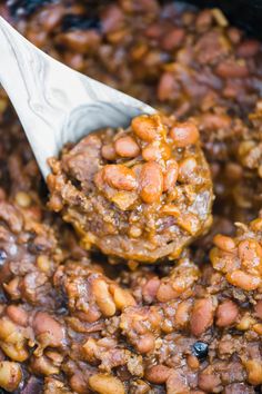 baked beans and meat are being stirred with a ladle in a slow cooker