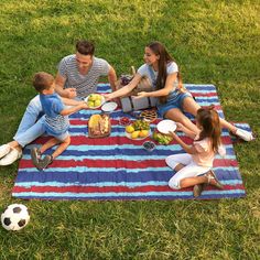 a family having a picnic on a blanket in the grass with fruit and vegetables around them