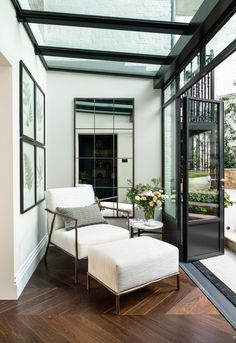 a white chair and footstool in a room with glass walls, wood flooring and large windows