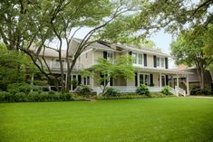 a large white house sitting on top of a lush green field in front of trees