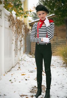 a woman in black and white striped shirt standing on snow covered ground next to fence