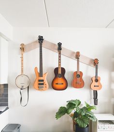 five guitars are hanging on the wall next to a potted plant and record player