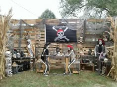 a group of people dressed up as skeletons in front of a wooden fence with a pirate flag