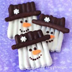 three marshmallow snowmen are decorated with chocolate and white icing on a purple background