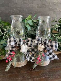 two glass vases with plaid bows are sitting on a table next to greenery