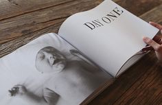 a person is holding an open book on a wooden table with the cover pulled down