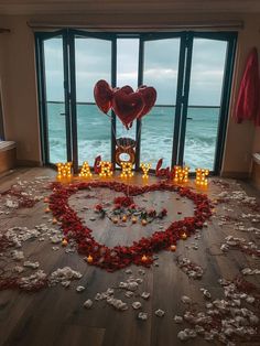 a heart shaped arrangement with candles and flowers on the floor in front of a large window