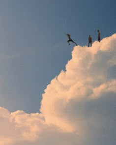 three people standing on top of a cloud in the sky with one person flying through the air