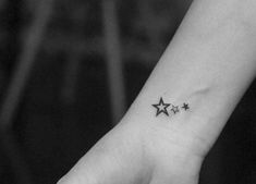 a small star tattoo on the wrist is shown in black and white, with three smaller stars