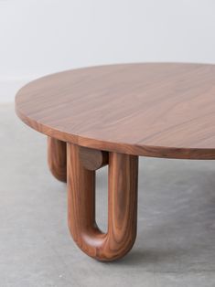 a wooden table with two circular legs and an oval shaped top, sitting on concrete flooring