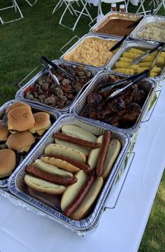 hot dogs, hamburgers and other foods are on display in trays at an outdoor event