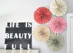 four paper fans are hanging on the wall next to a sign that says life is beauty full