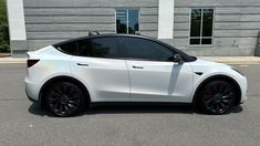 a white tesla car parked in front of a building with black wheels and rims