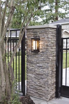 a light that is on the side of a stone wall next to a tree and fence