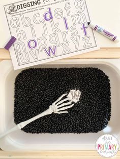 a plastic container filled with black beans next to a white and purple letter writing activity