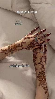 a woman's hands with henna on top of a bed covered in white sheets