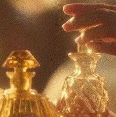 a person is holding a glass bottle in front of a small golden object on a table