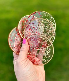 a hand holding three coasters with glitter on them in front of a green field