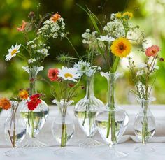 four vases filled with different types of flowers on top of a white table cloth