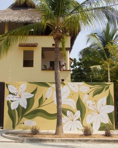 a palm tree in front of a painted wall with white flowers and leaves on it