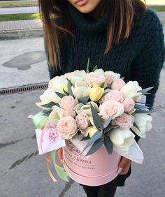 a woman holding a pink box with flowers in it and a tag on the side