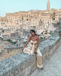 a woman sitting on top of a stone wall next to a city filled with buildings