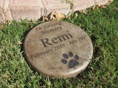 a memorial stone with a paw print on it in the grass next to a brick wall