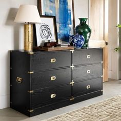 a black and gold dresser in a living room with art on the wall behind it