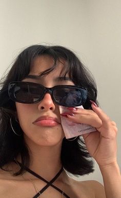 a woman with sunglasses on her face holding up a piece of paper to her eye