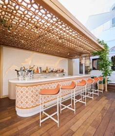 an outdoor bar with orange stools and wooden flooring, along with potted plants