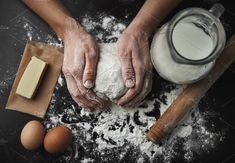 two hands are kneading dough on top of flour next to an egg and butter shaker