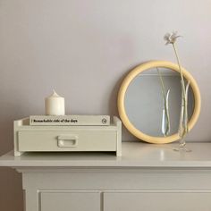 a table with a mirror, vase and candle on it next to a white dresser