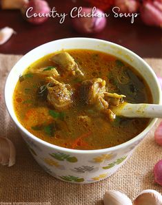 a bowl of soup with meat and vegetables on the table next to some garlic cloves