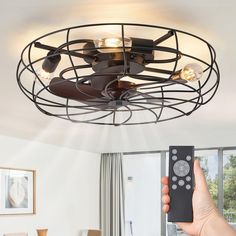 a person holding a remote control up to a ceiling fan that is attached to a light fixture