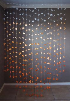 an art installation with orange and white leaves hanging from it's sides on a gray wall