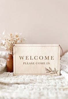 a welcome sign sitting on top of a bed next to a vase filled with flowers