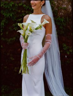 a woman in a white wedding dress holding a bouquet of flowers and wearing a veil