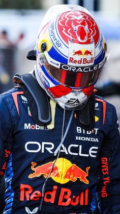 a man with a helmet on and ear buds in his ears is wearing a red bull racing uniform