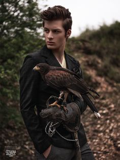 a man holding an eagle on his arm in front of some trees and dirt ground