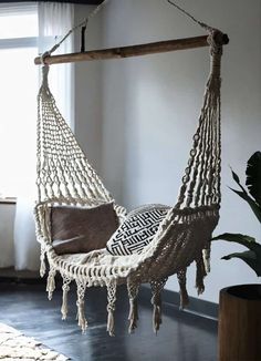 a white hammock hanging from a wooden pole in a room with a potted plant