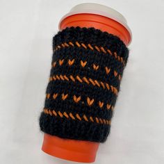 a knitted cup sleeve with an orange and black design on it, sitting on a white surface