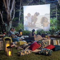 people sitting on the grass watching a movie in front of a large screen with candles