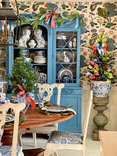 a dining room table with blue and white china cabinet in the background, surrounded by floral wallpaper