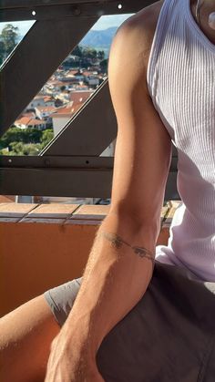 a man sitting on top of a wooden bench wearing a white tank top and grey shorts