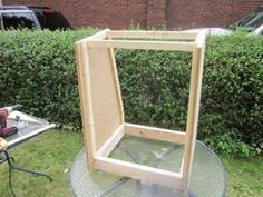 a wooden frame sitting on top of a glass table next to a hedge and car