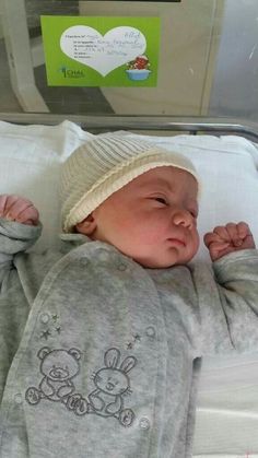 a baby is laying in a hospital bed wearing a white hat and grey onesie