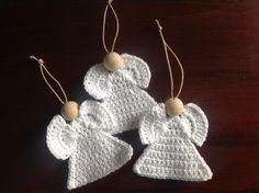 three crocheted angel ornament hanging on a wooden table with two wood beads