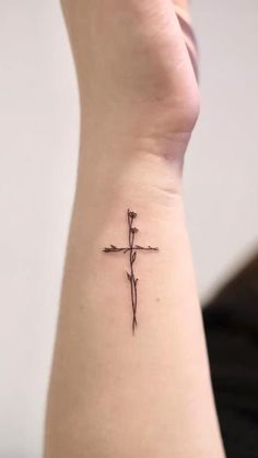 a small cross tattoo on the left side of the arm is shown in black ink