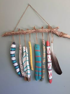 several different colored feathers hanging from a wooden branch on a gray wall with a string attached to it